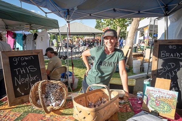Katy Chandler standing at her booth with a shirt that says "FARMY" in an ARMY logo style